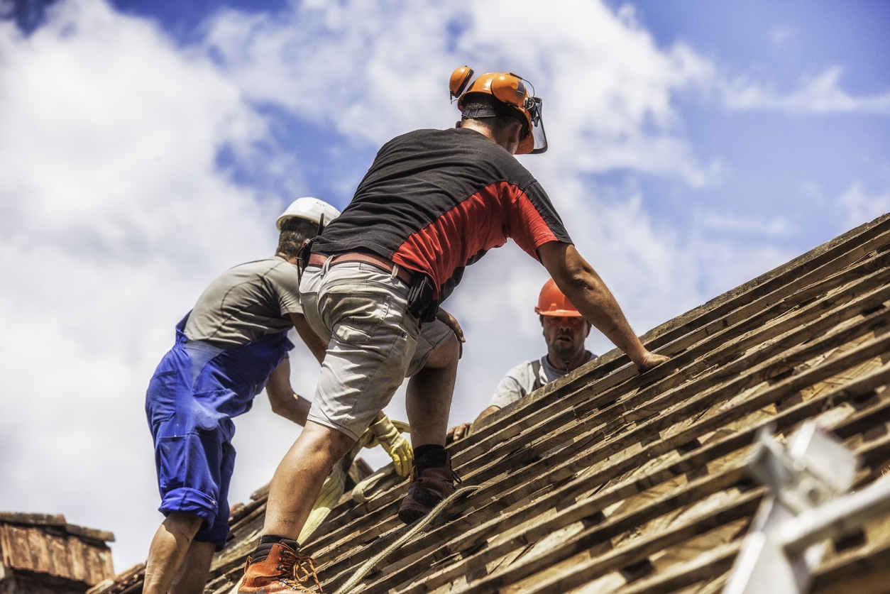 Three men working on a wooden roof renovating a house.