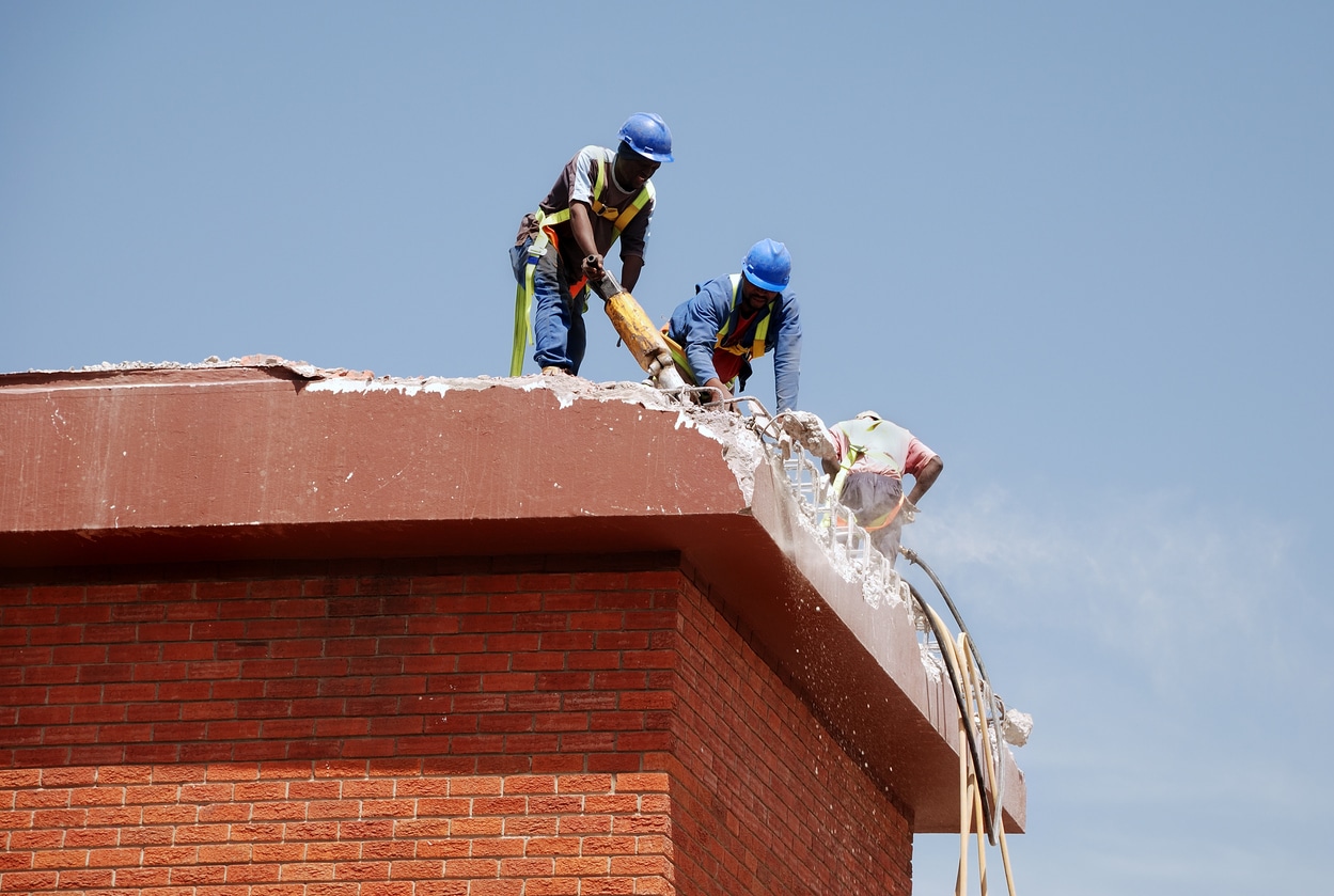 three men tearing off concrete roof